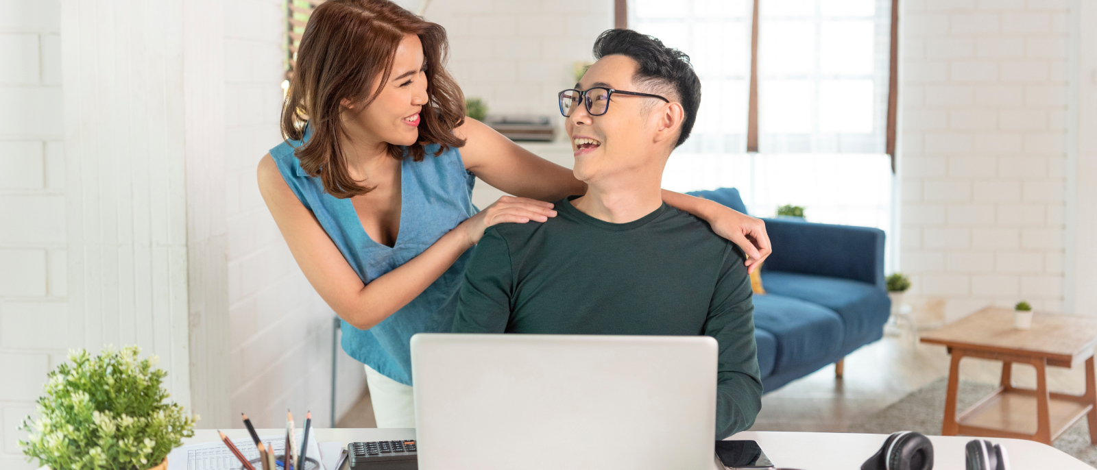 A young couple on a laptop smiling at each other (because they've just learned what is included in a mortgage payment).